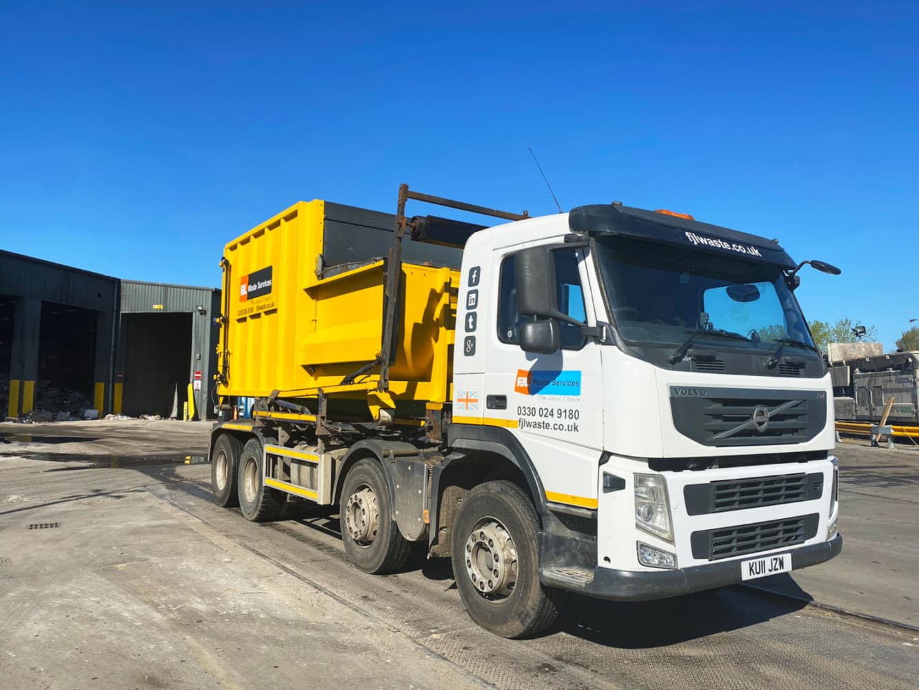 FJL Waste Services Volvo hookloader lorry with yellow compactor in the yard